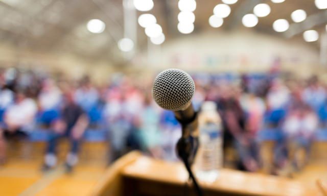 Close-up of a microphone on a podium with a blurry crowd of people in the background.