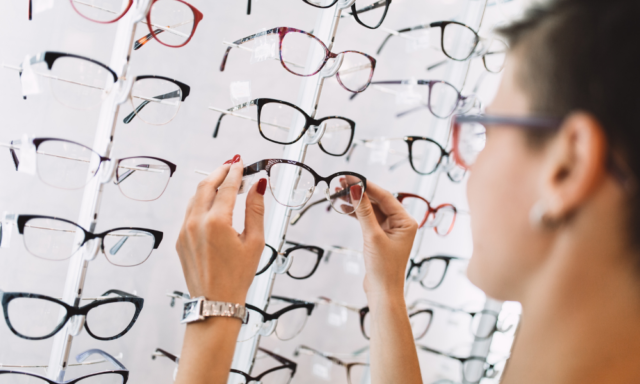 Woman lifting a pair of glasses from a display in an optical store