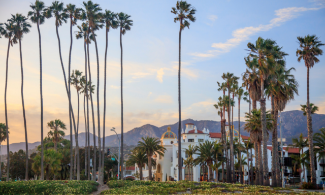 View of Santa Barbara, CA with palm trees and buildings and a mountain backdrop.