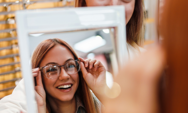 a woman trying on glasses, looking in a mirror at an optical