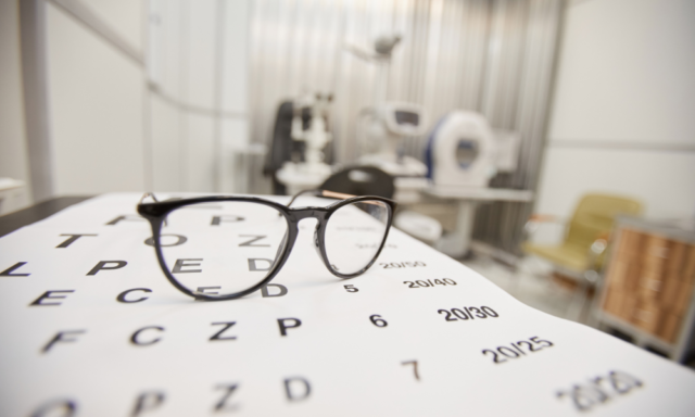 a pair of glasses sits on top of an eye chart in an exam room