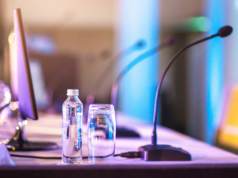 The Optometry Conferences We’re Eyeing in 2025 view of a conference panel table with microphones and water bottles