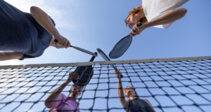 JAN 23 – 25 | ISVA 2025 View from below of 4 people tapping pickleball rackets together over a net