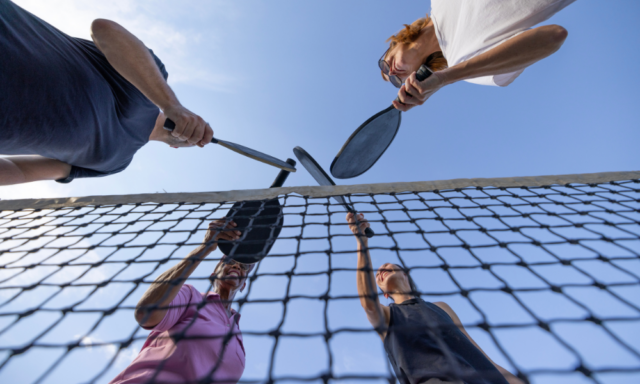 View from below of 4 people tapping pickleball rackets together over a net