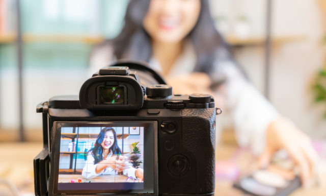 Camera recording video with a woman at a desk in the background