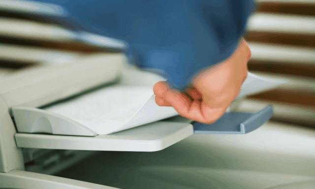 hand grabbing paper out of a fax machine tray