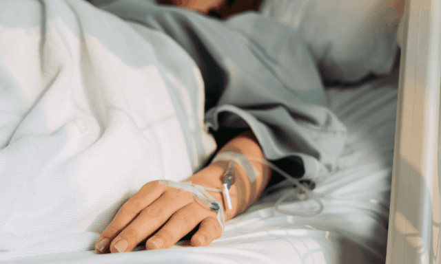 View of the hand of a person in a hospital bed, hooked up to an IV